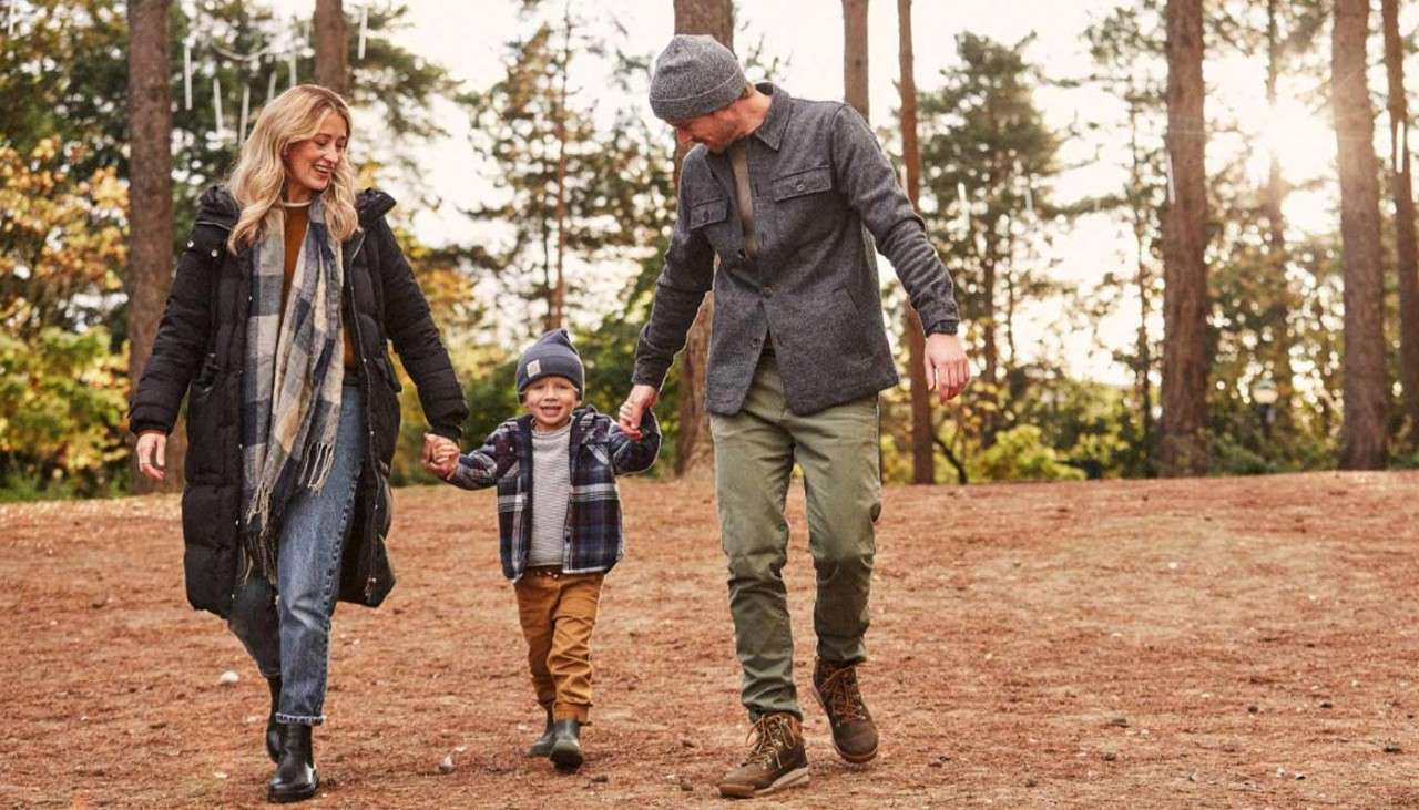 A mother and father with their young son holding hands and walking together through the forest in Autumn.