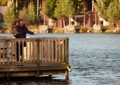 A parent and child on a pier looking at the lake.