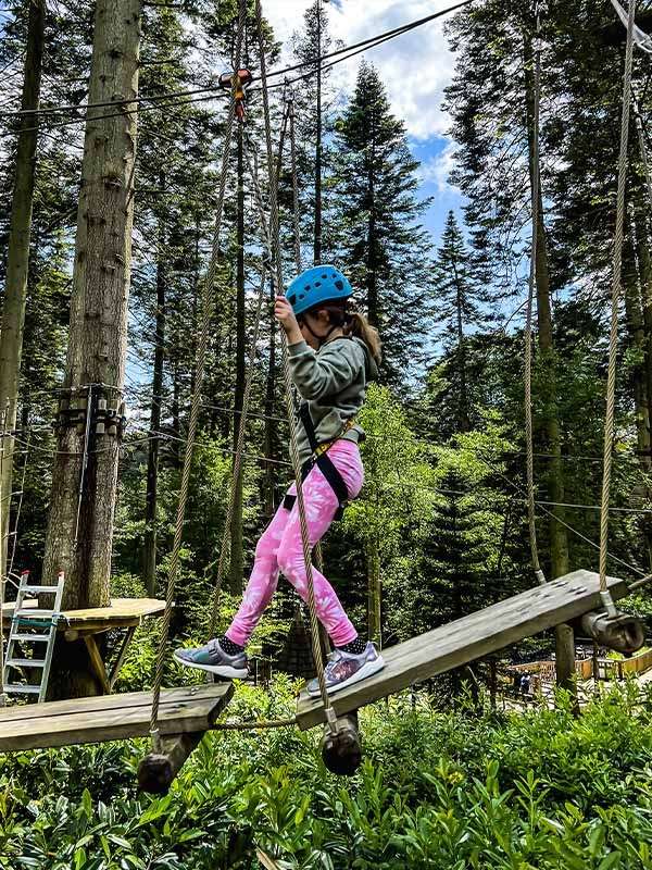 A girl wearing a harness completing the aerial adventure obstacle course in the trees.