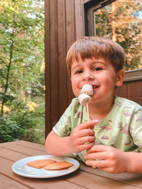 A little boy sat outside his lodge eating a marshmallow.