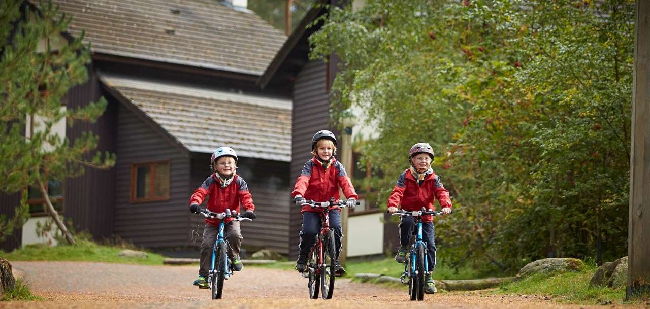 Three boys on cycles through Center Parcs with lodges behind them