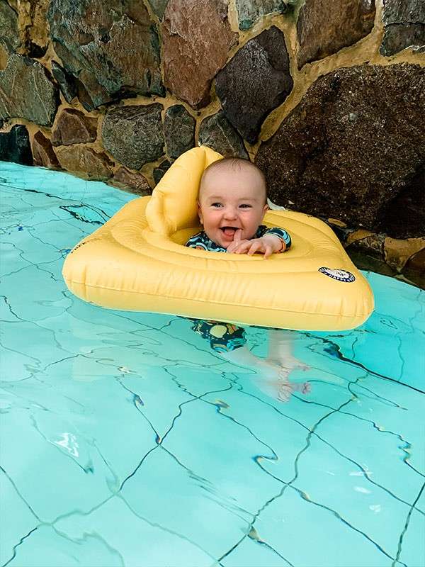 A baby in an inflatable in the pool smiling at camera.