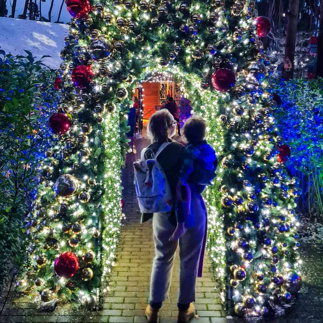 A mother holding her son whilst walking through winter light display.