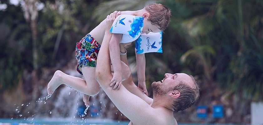 Father lifting his son in the pool. The boy wears Center Parcs arm bands.
