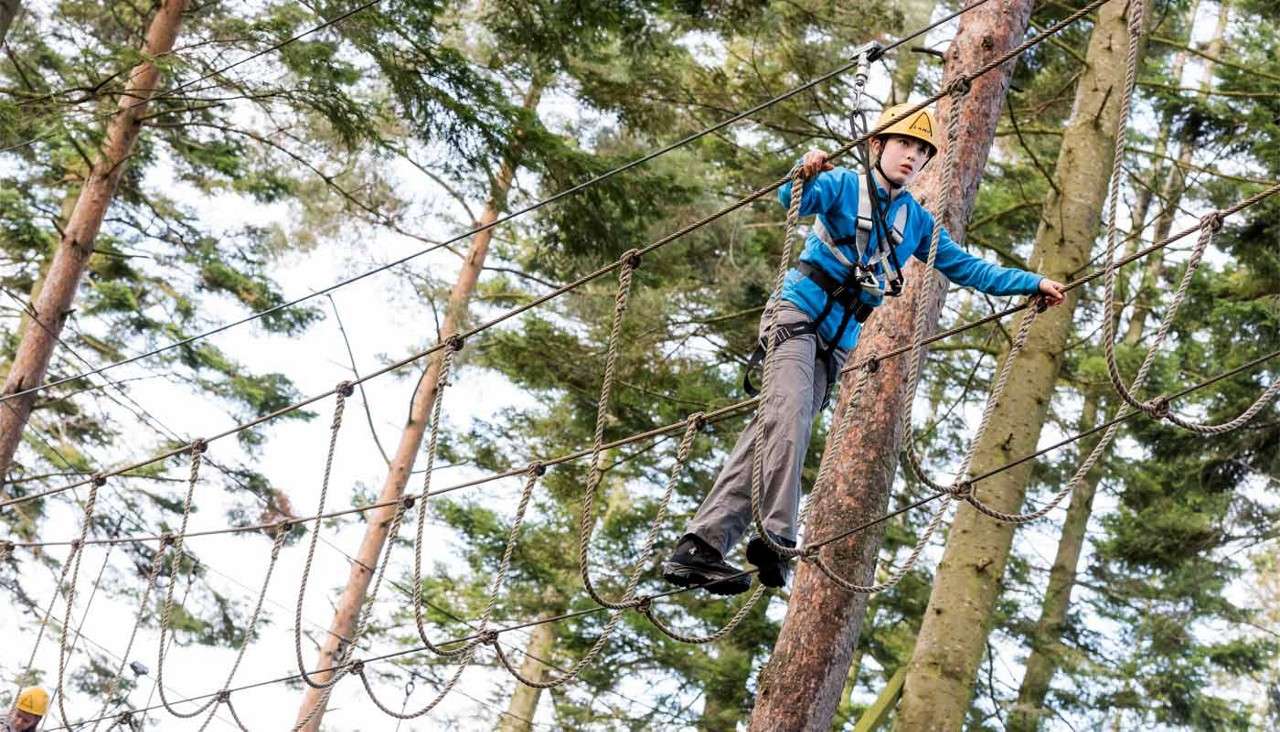 A young person walking a suspended rope bridge