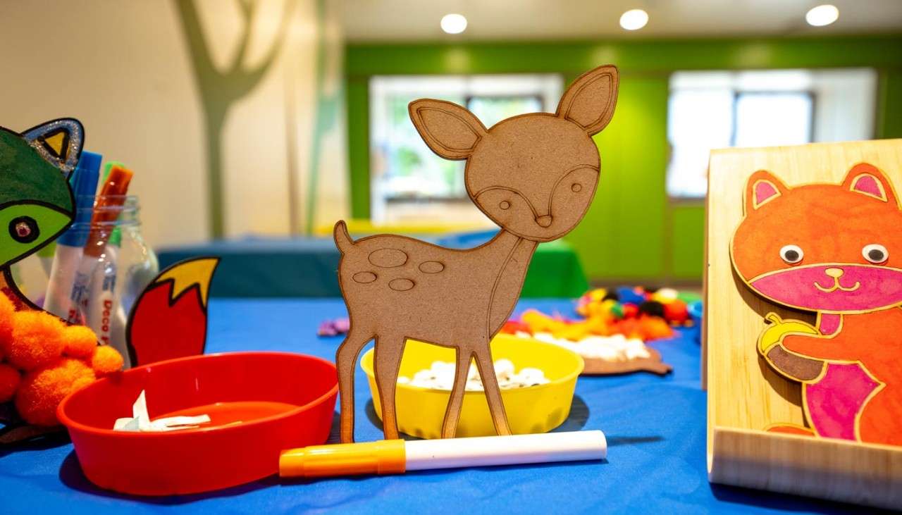 Mini wooden deer surrounded by colourful craft materials.