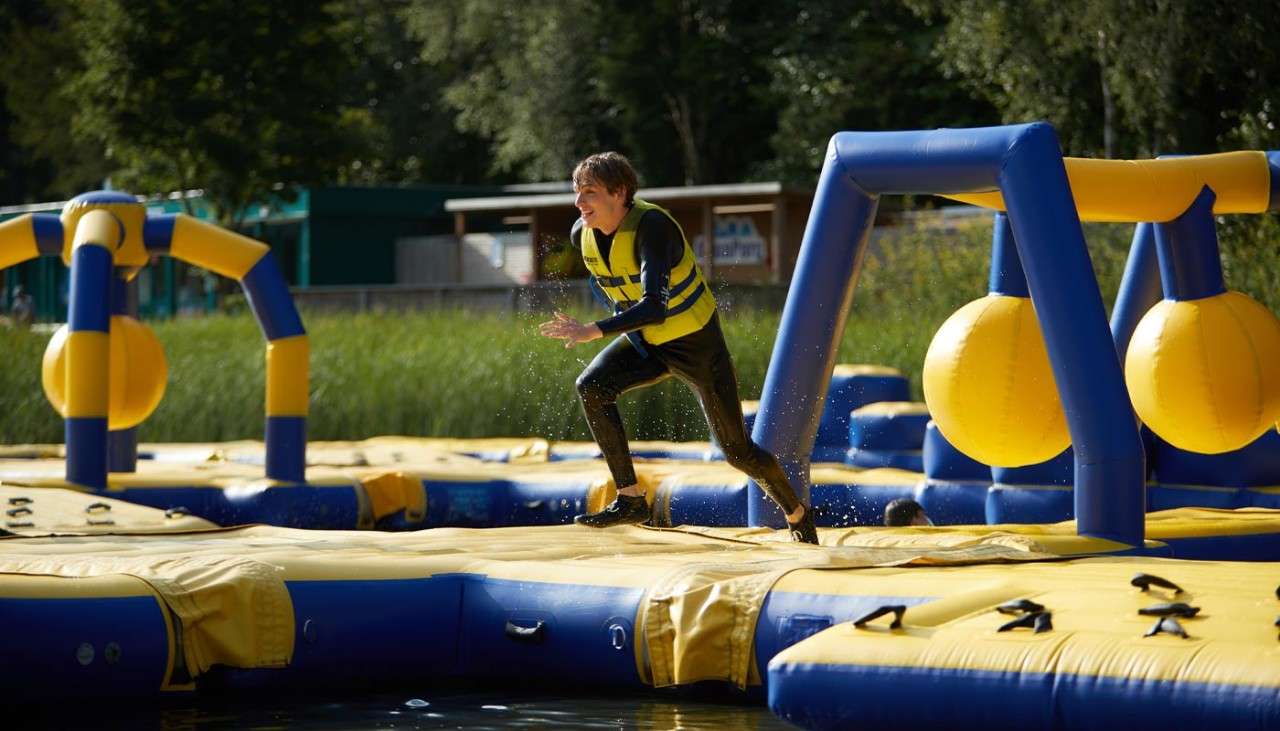 Teenage boy running over an inflatable obstacle course on the lake.