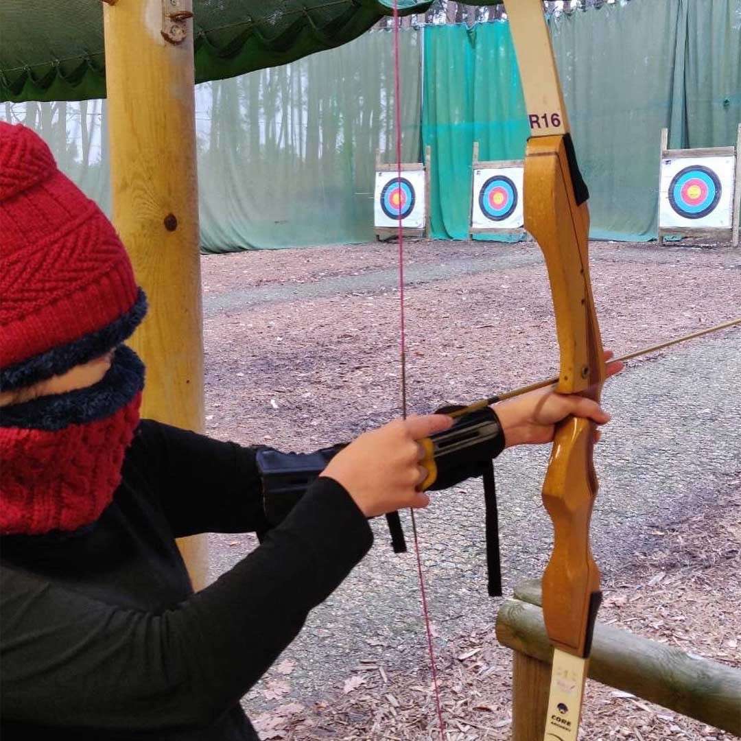 Young boy wearing a winter hat aiming a bow and arrow.