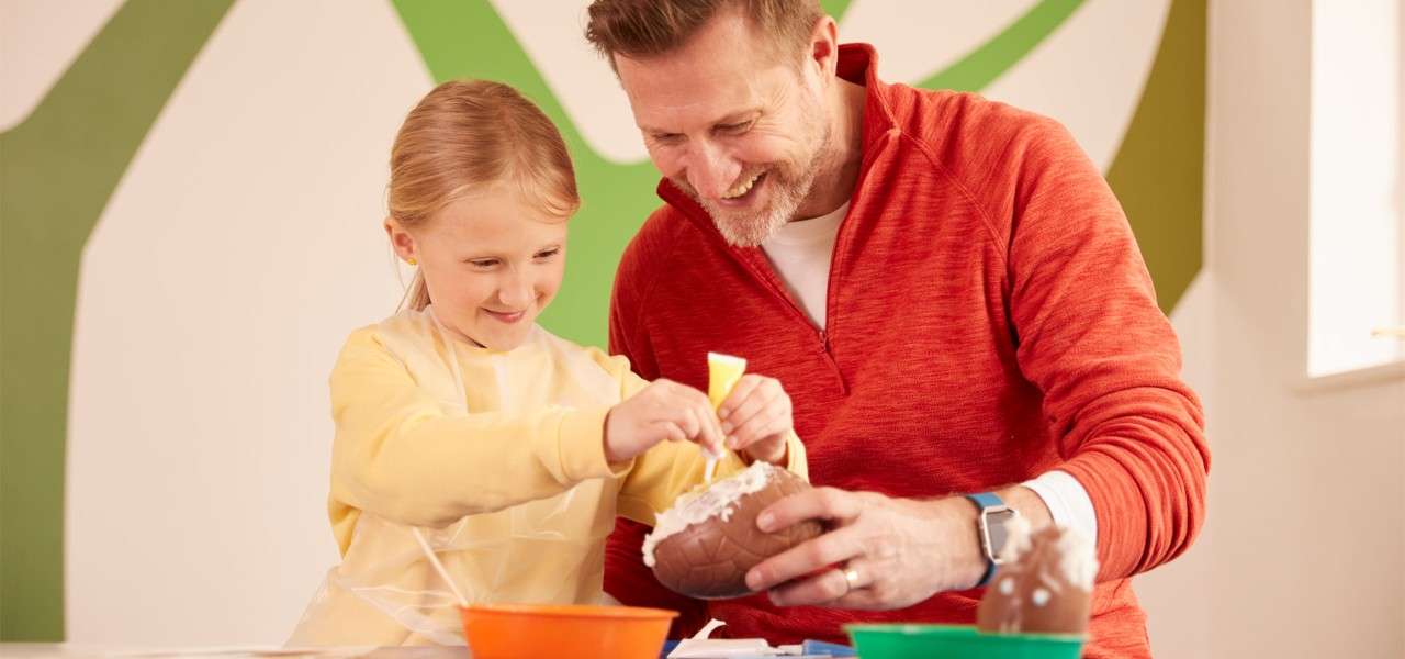 Father and daughter decorating a chocolate egg.