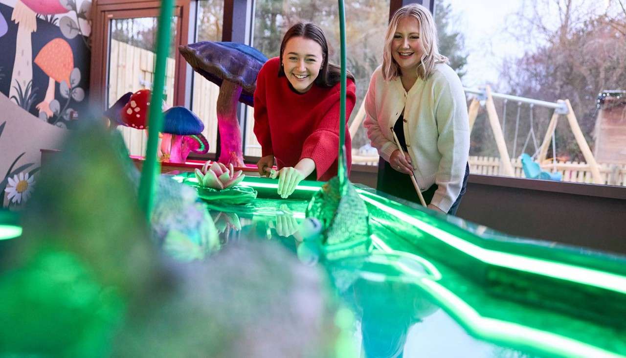 Two women playing Crazy Pool on a glowing table.