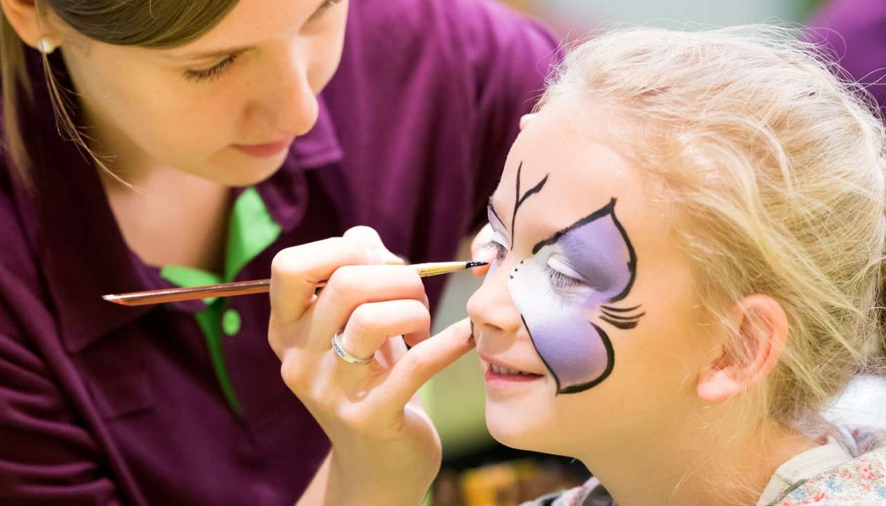 Lady painting a butterfly on a young girls face