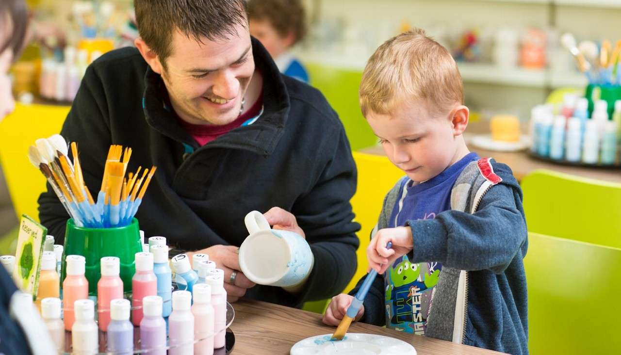 Young boy with his dad painting pots.