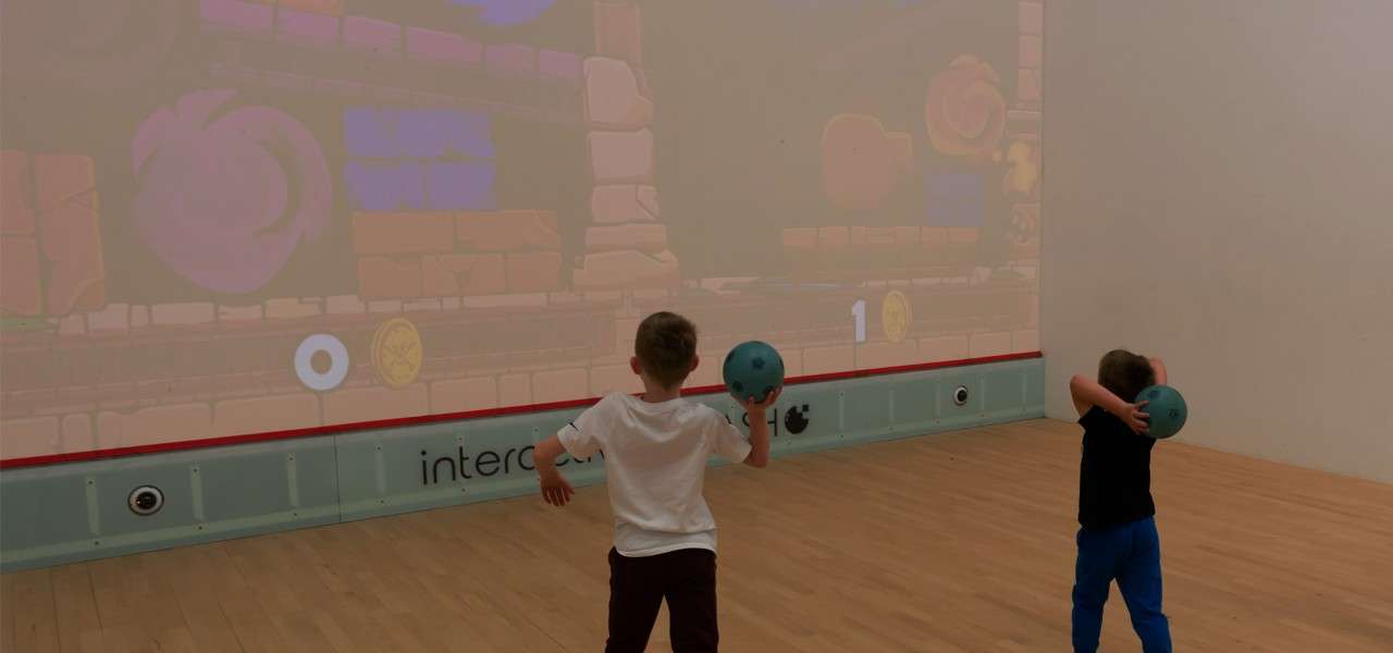 2 children throwing balls at an interactive wall