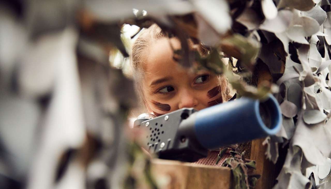 Young girl aiming a laser gun through a camouflage net