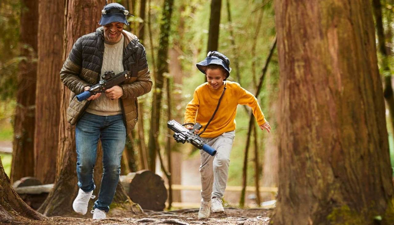 Man and child running through the trees holding Laser Combat guns