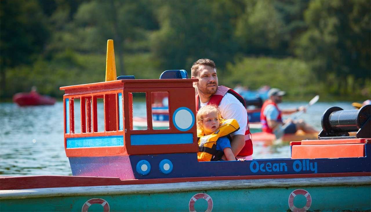 Man and a young girl sailing in a colourful boat on the lake.