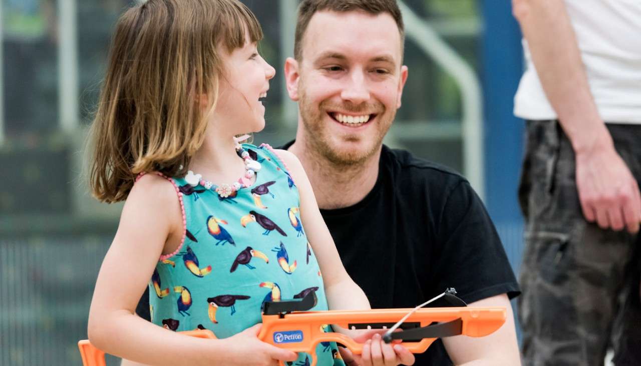 Young girl holding a Mini Crossbow whilst laughing with an adult