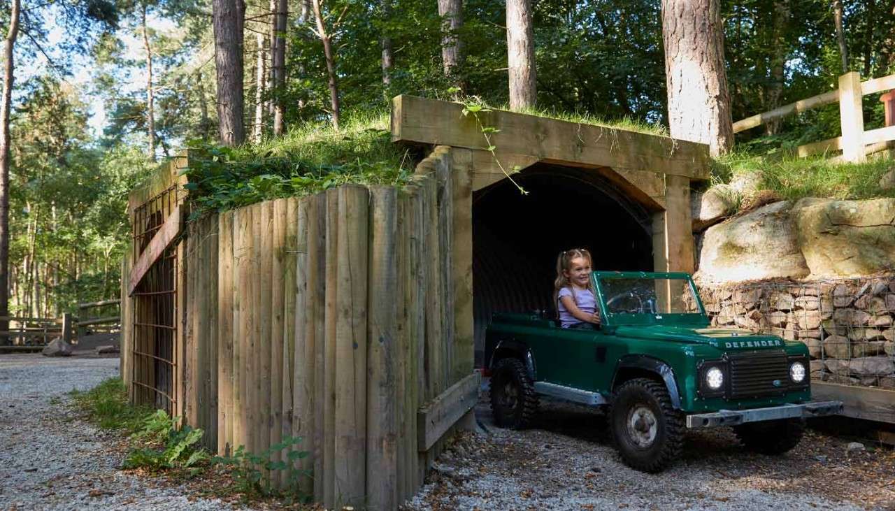 Young girl driving a small car through a wooden tunnel