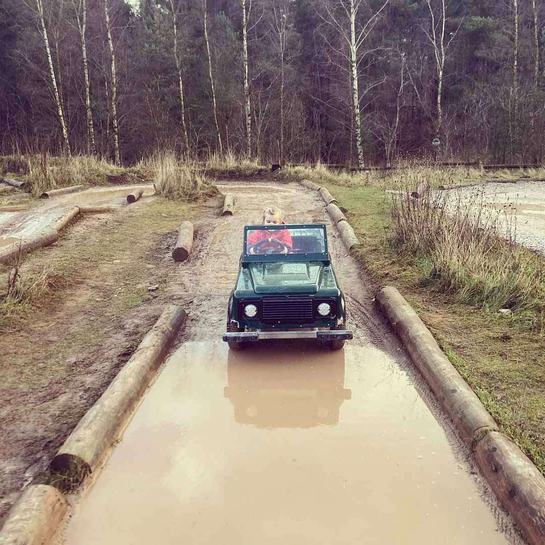 Young girl driving a little car through a large puddle.