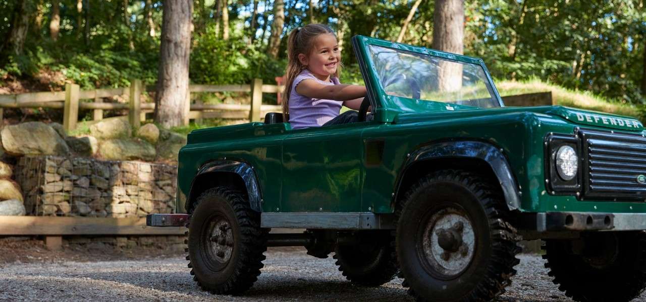 Young girl driving a little car through the forest.