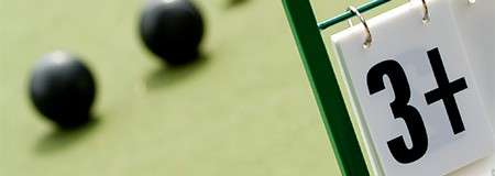 Score marker displays “3+”, positioned next to several black lawn bowls resting on a green playing surface.