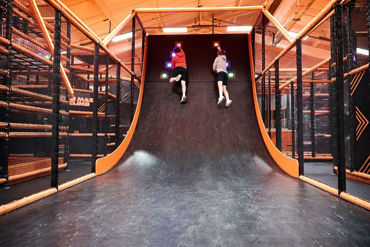 Two people reaching up a slopped wall.