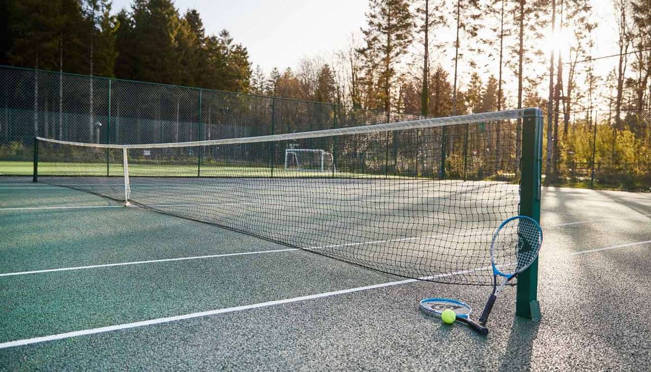Tennis racket and ball leaned up against a Tennis net