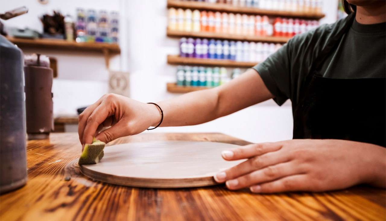 Person using a sponge to apply a wood stain to a circular piece of wood.