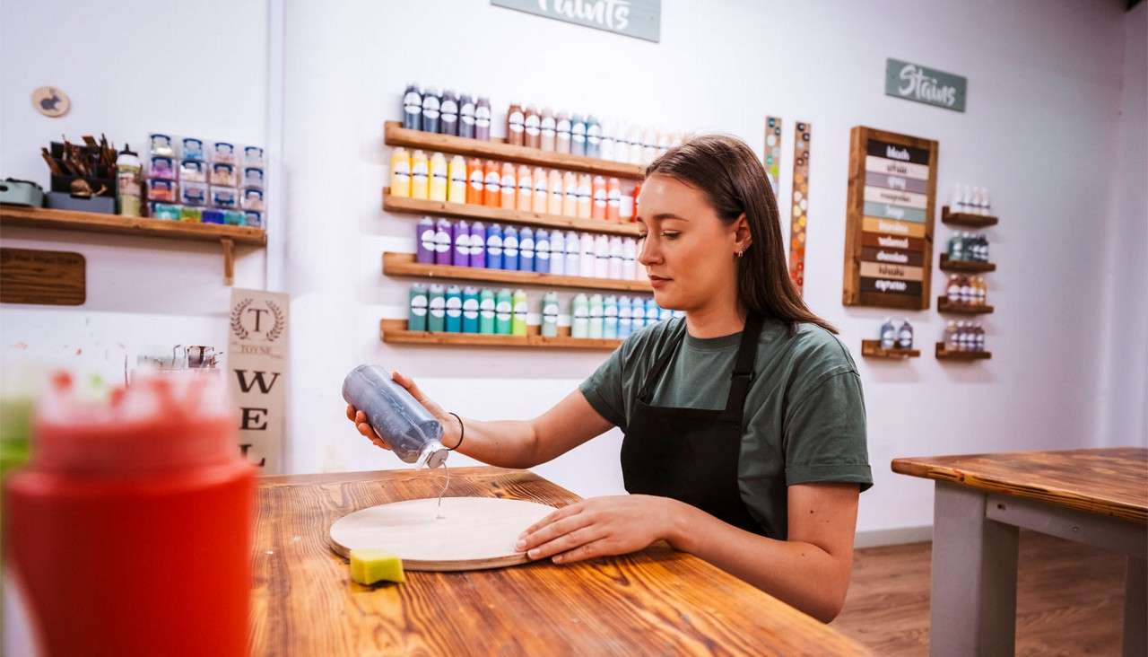 Woman pouring a wood stain onto a wooden plaque.
