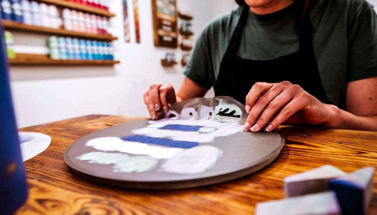 Woman aligning a stencil on a wooden plaque.