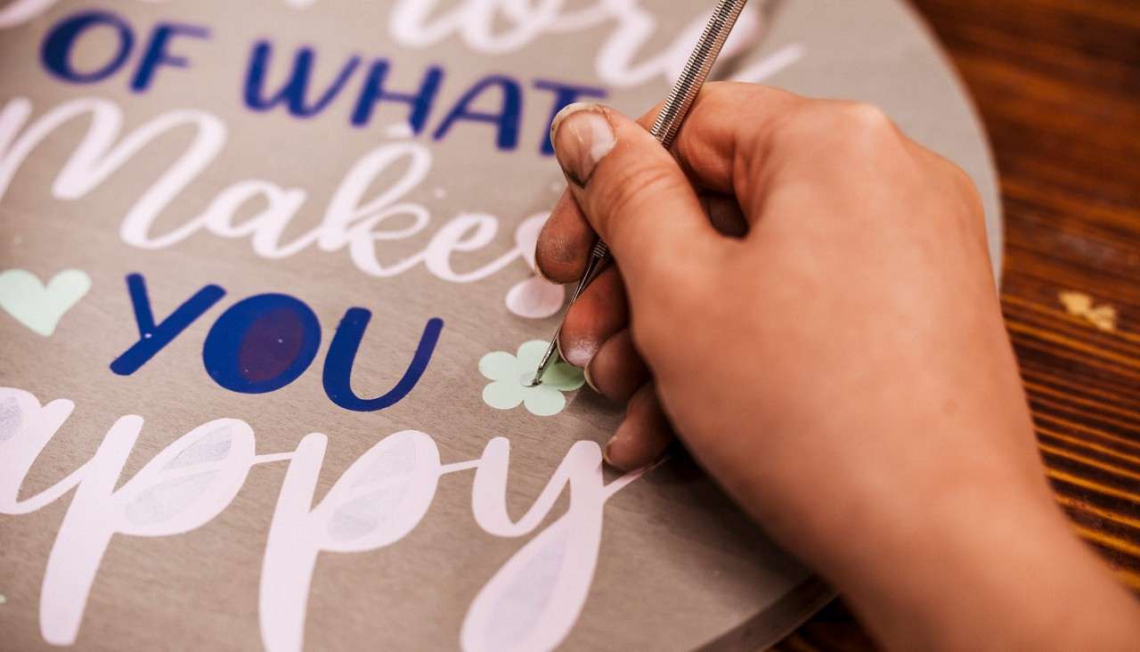 Person peeling away a stencil from a wooden plaque.