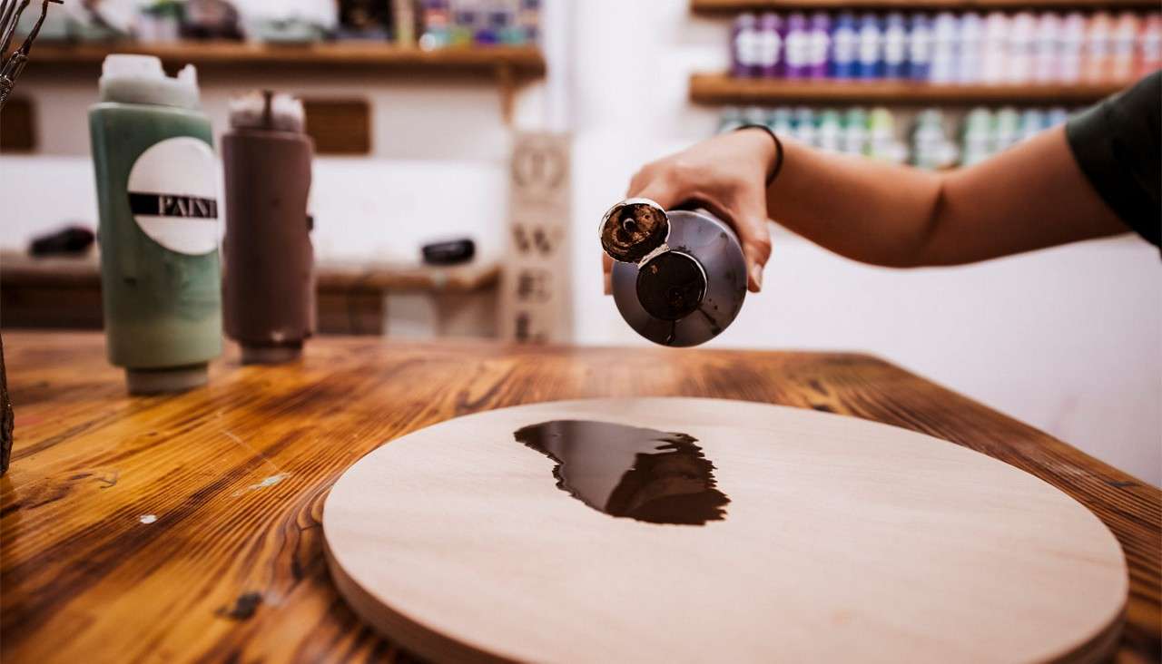 Pouring a wood stain onto a circular wooden board.