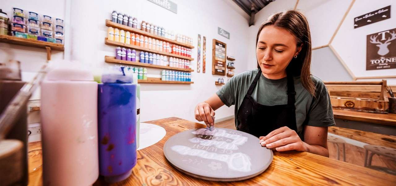 Woman staining a wooden sign in the Woodcraft Workshop.