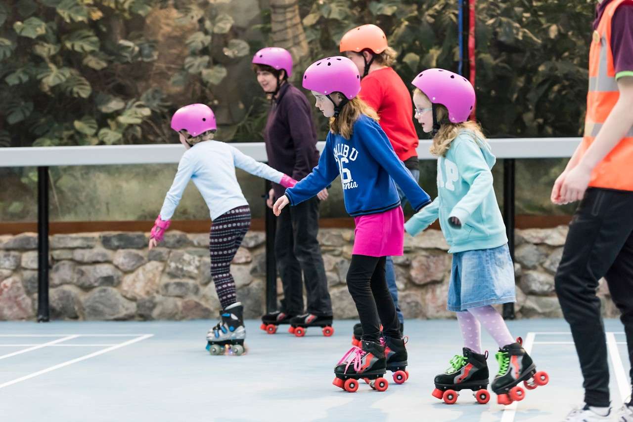 A group of girls roller skating with helmets on 