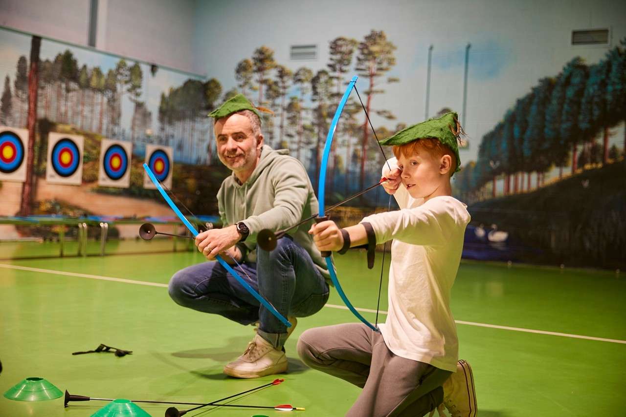 A boy wearing a Robin Hood hat and aiming his arrow