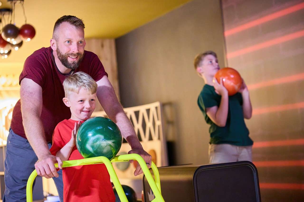 A man helping his son with the bowling ball