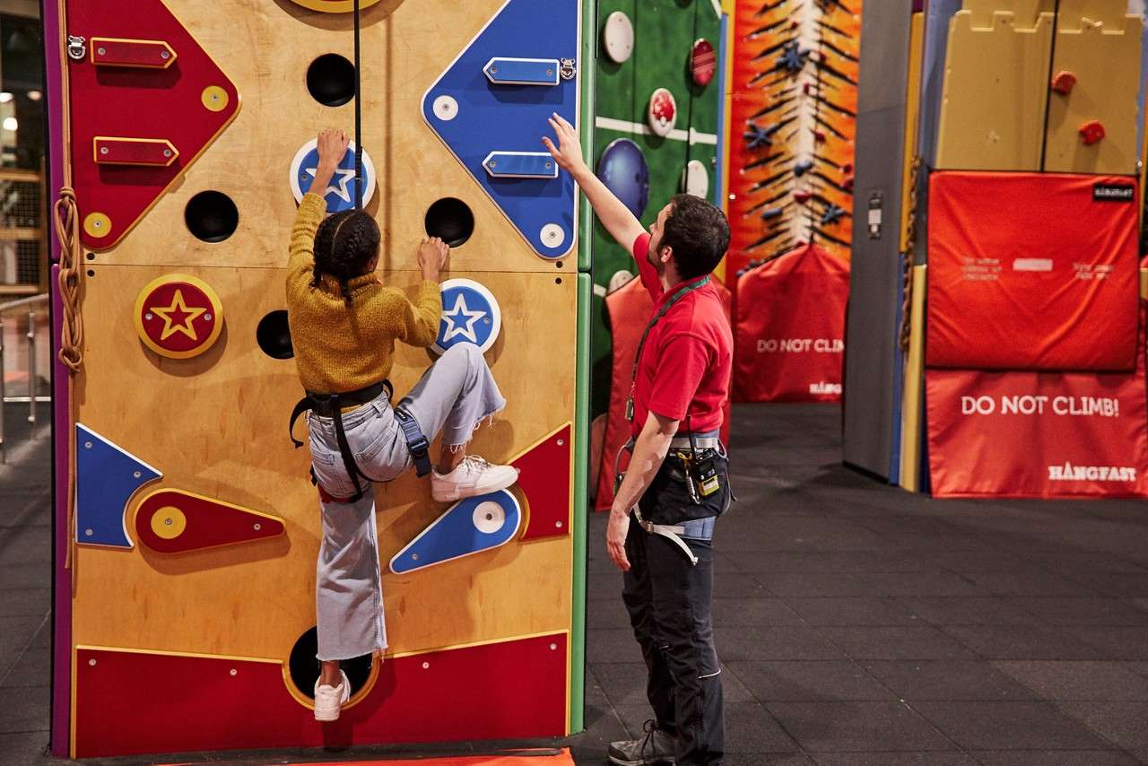 A teen starting to climb up the wall with her harness on