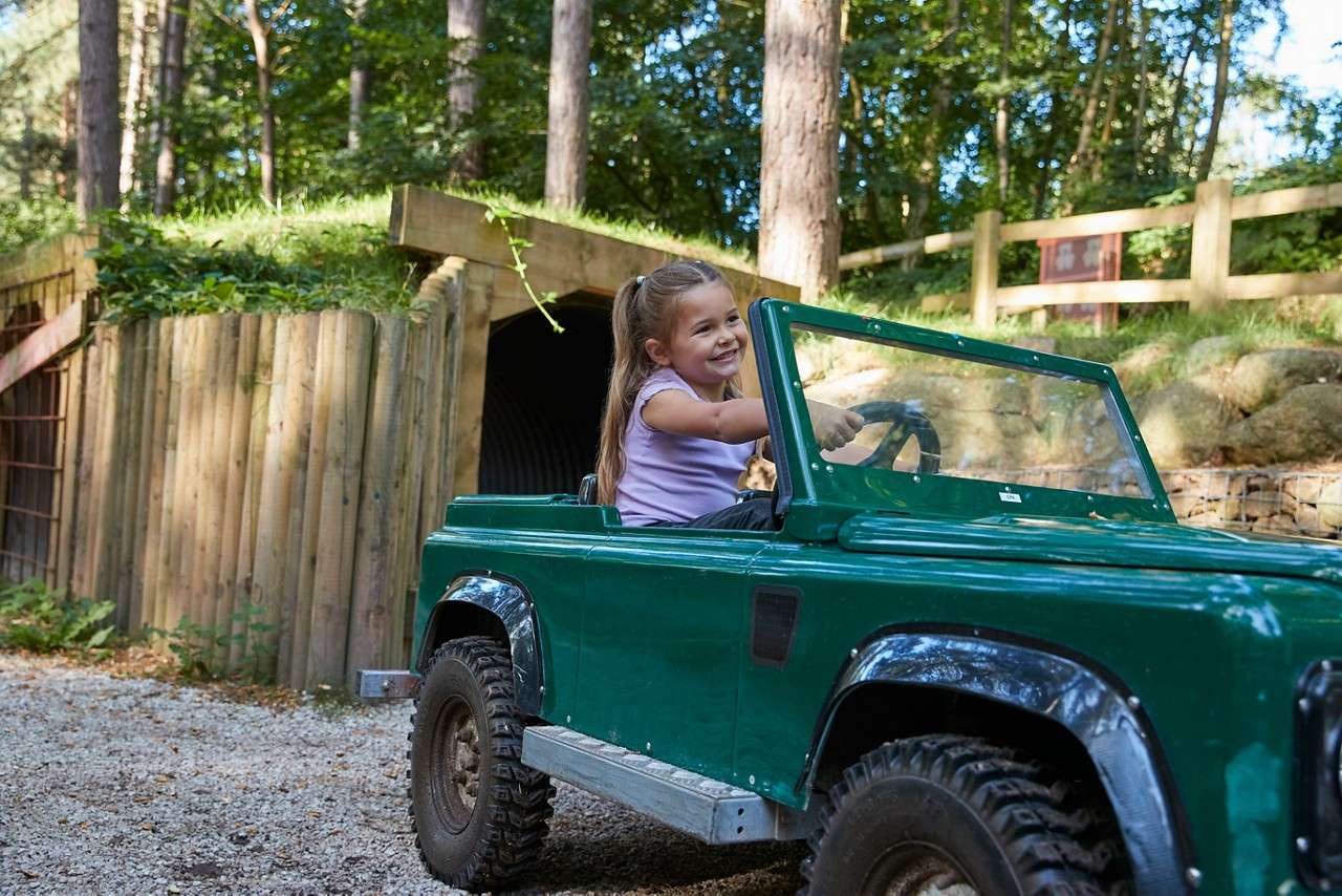 A little girl smiling and holding the wheel of her mini jeep