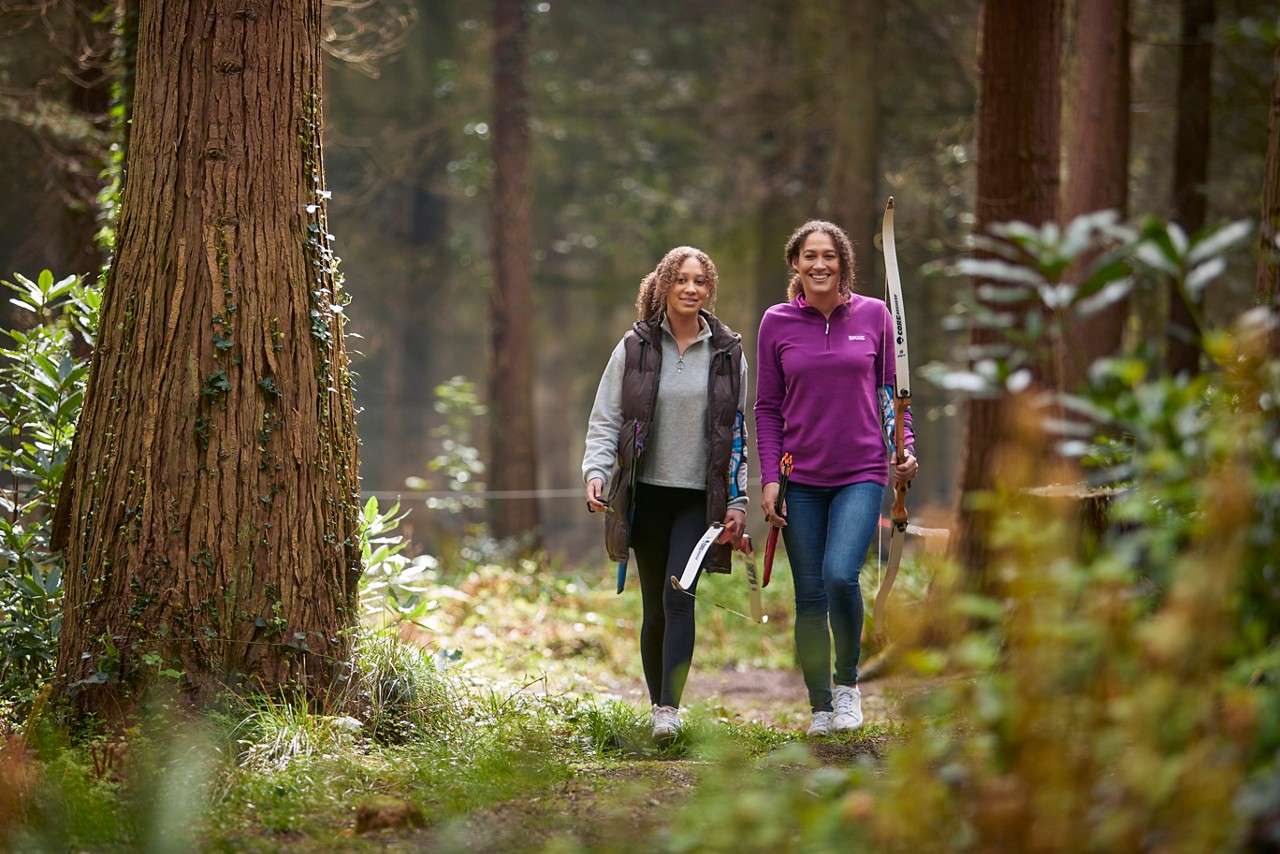 Two people walking through the forest with a bow and arrow