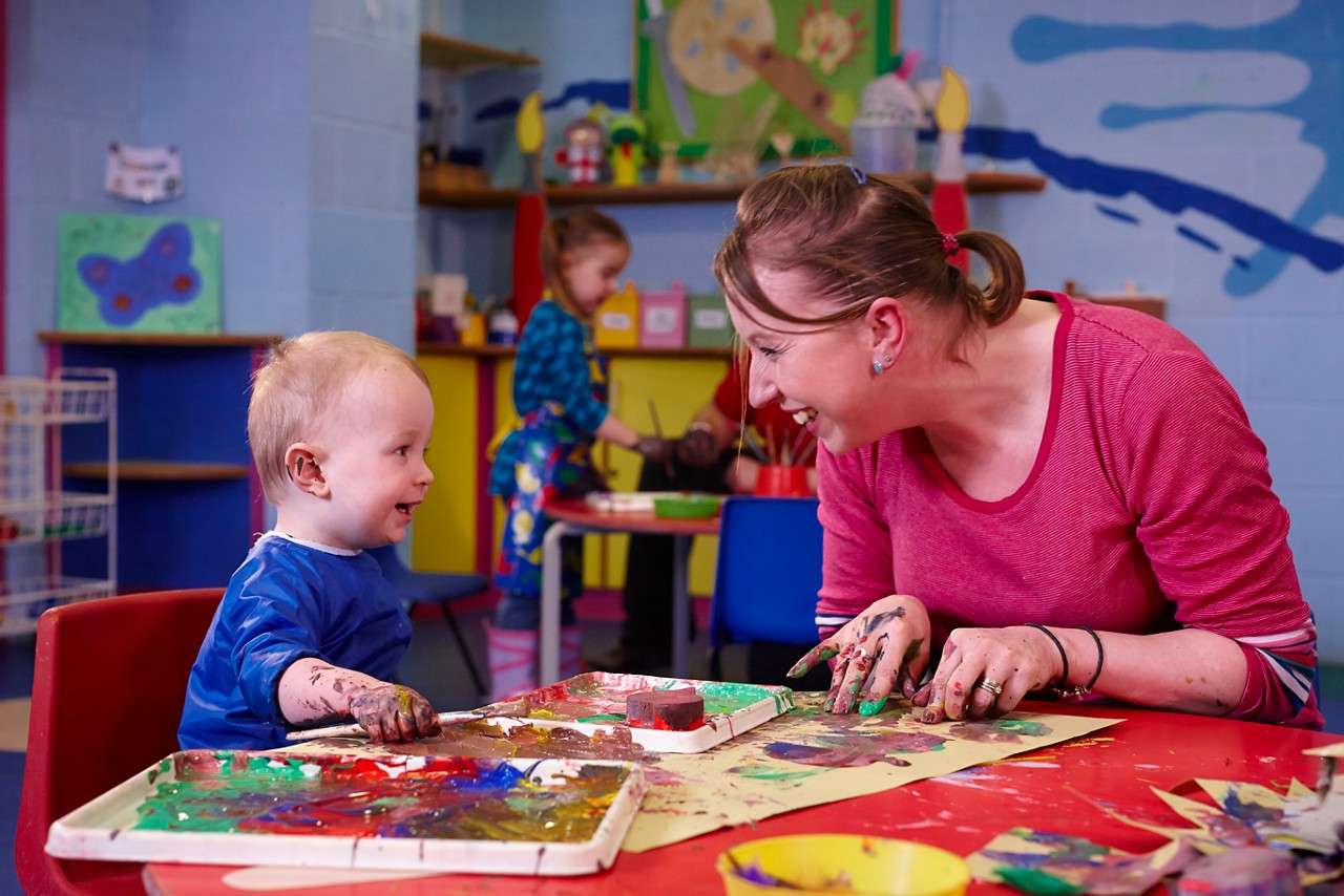 A mum and little boy sat at a table painting pictures