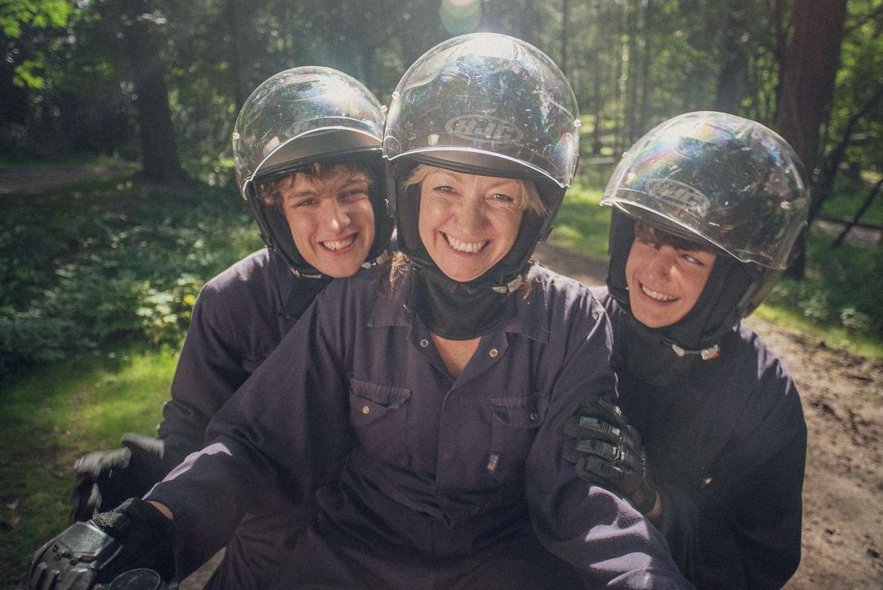 A mum and two sons smiling at the camera quad biking