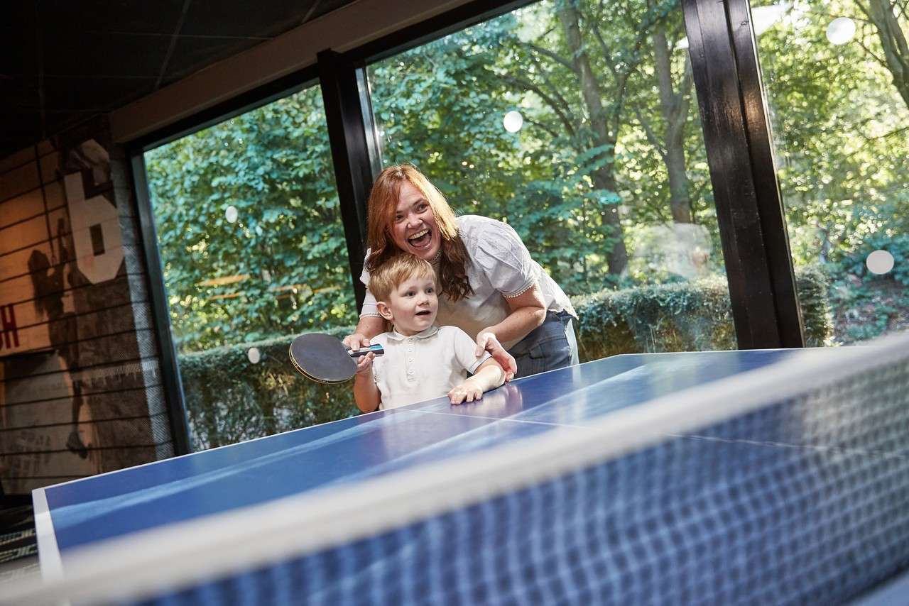 A toddler playing table tennis with his mum