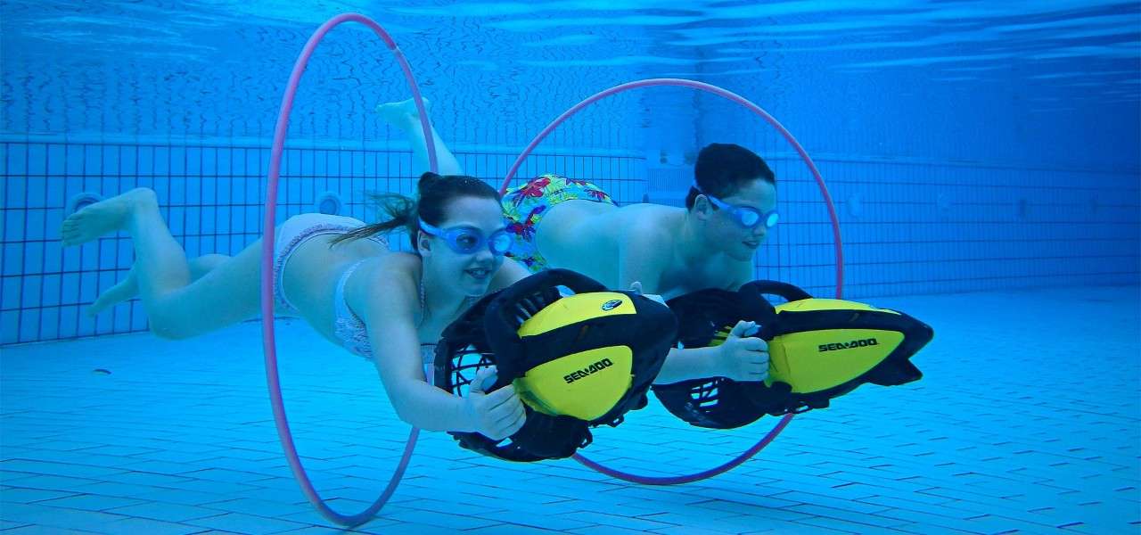 Two teenagers swimming underwater through hoops.