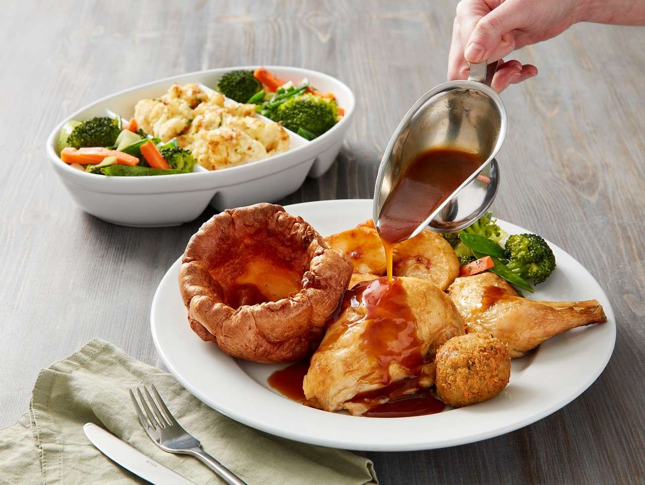 Hand pouring gravy on a roast chicken dish