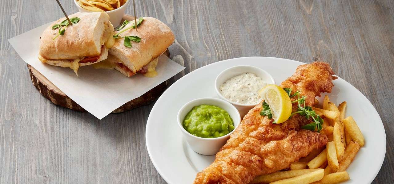A plate of fish and chips and a plate with a warm sandwich