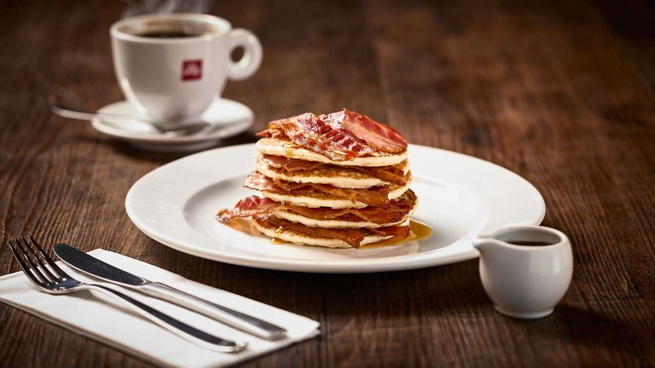 Classic American Pancake Stack topped with crispy bacon and drizzle.