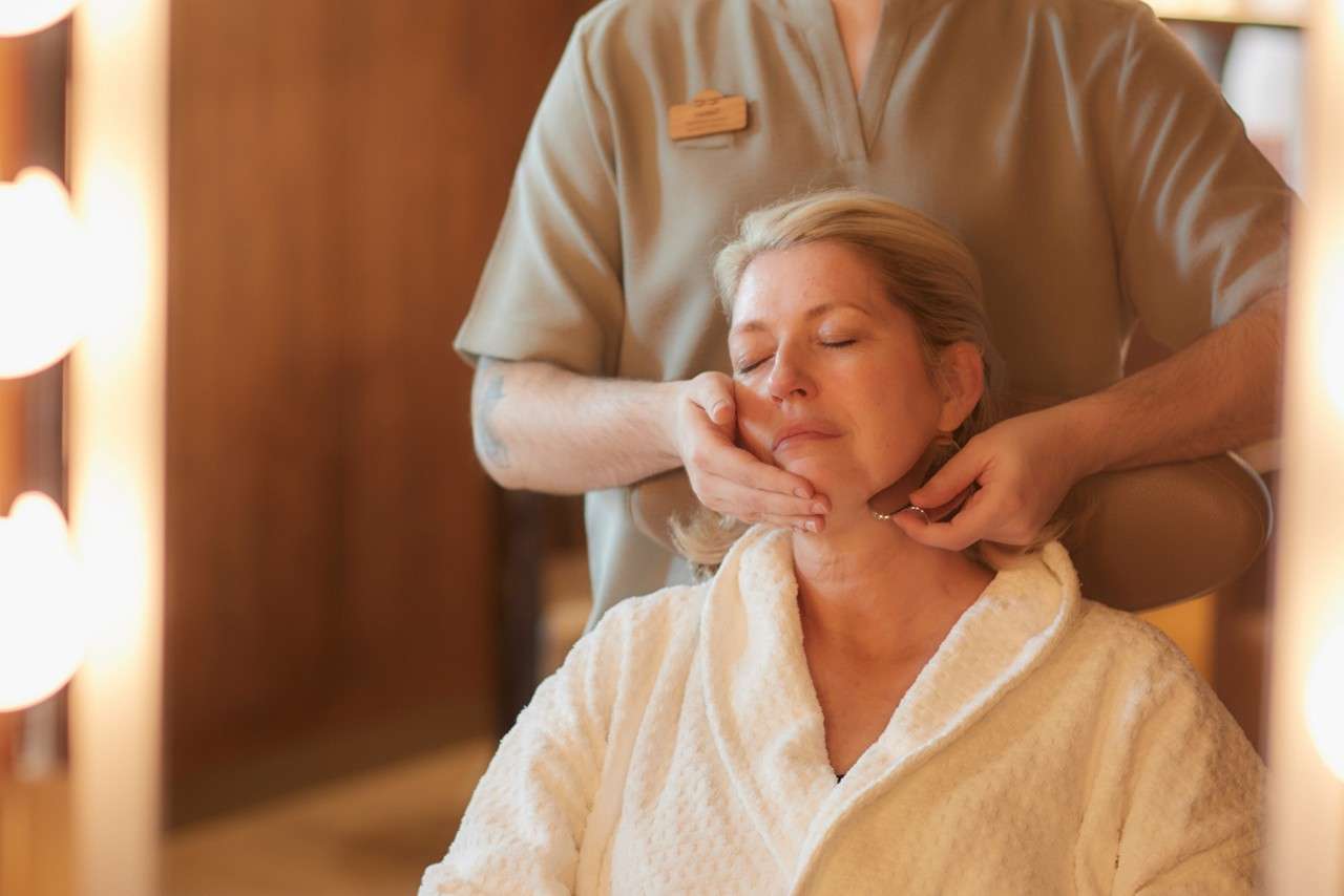 A lady wearing a robe having a facial treatment with a Gua Sha.