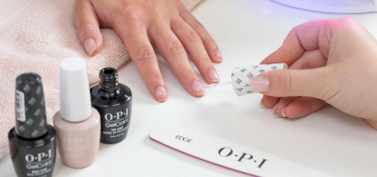 Hand receiving a manicure, nail polishes on the side.