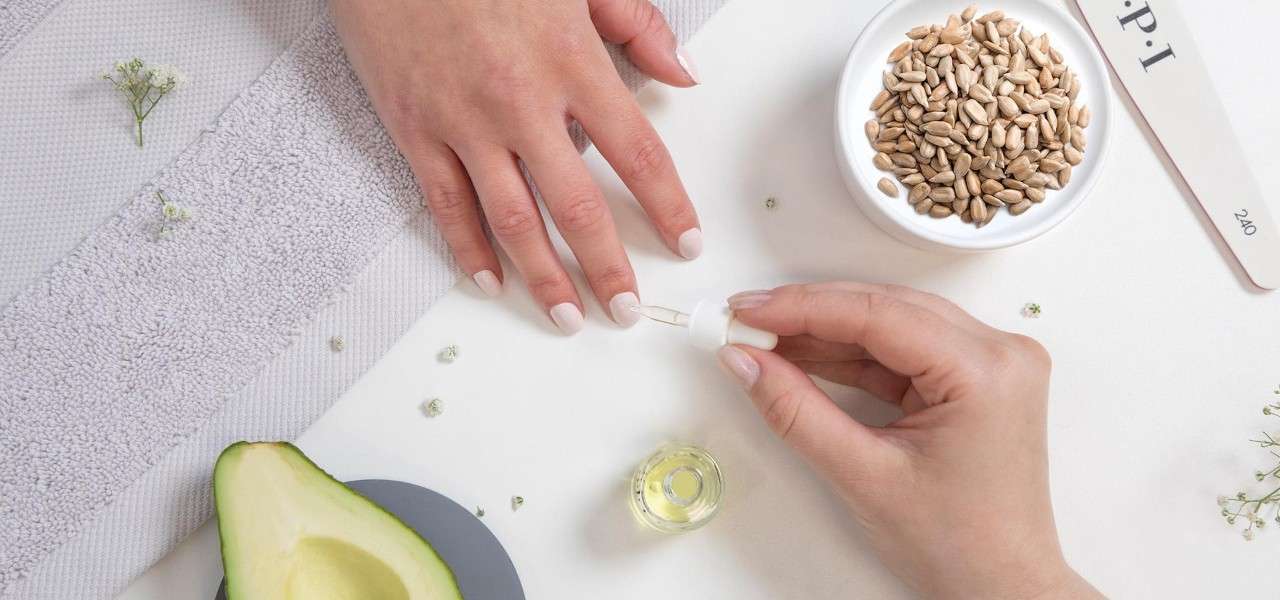 A hand receiving a manicure surrounded by a avocado half, polish and a nail file. 