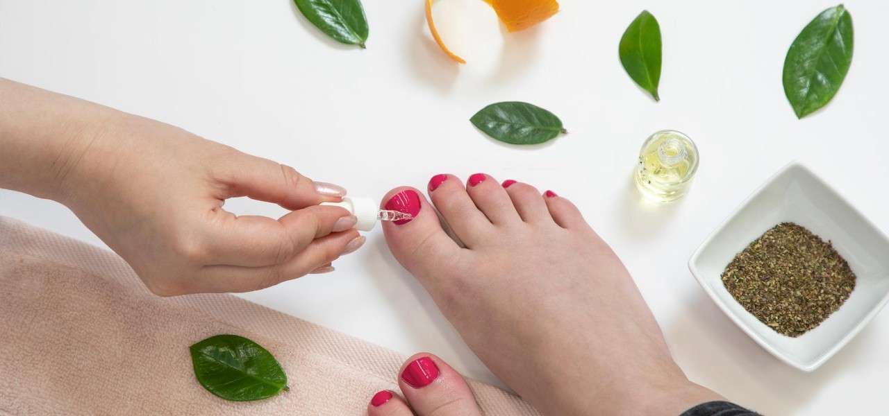 Two feet with red nail polish receiving a pedicure, surrounded by leaves, herbs and orange peel.
